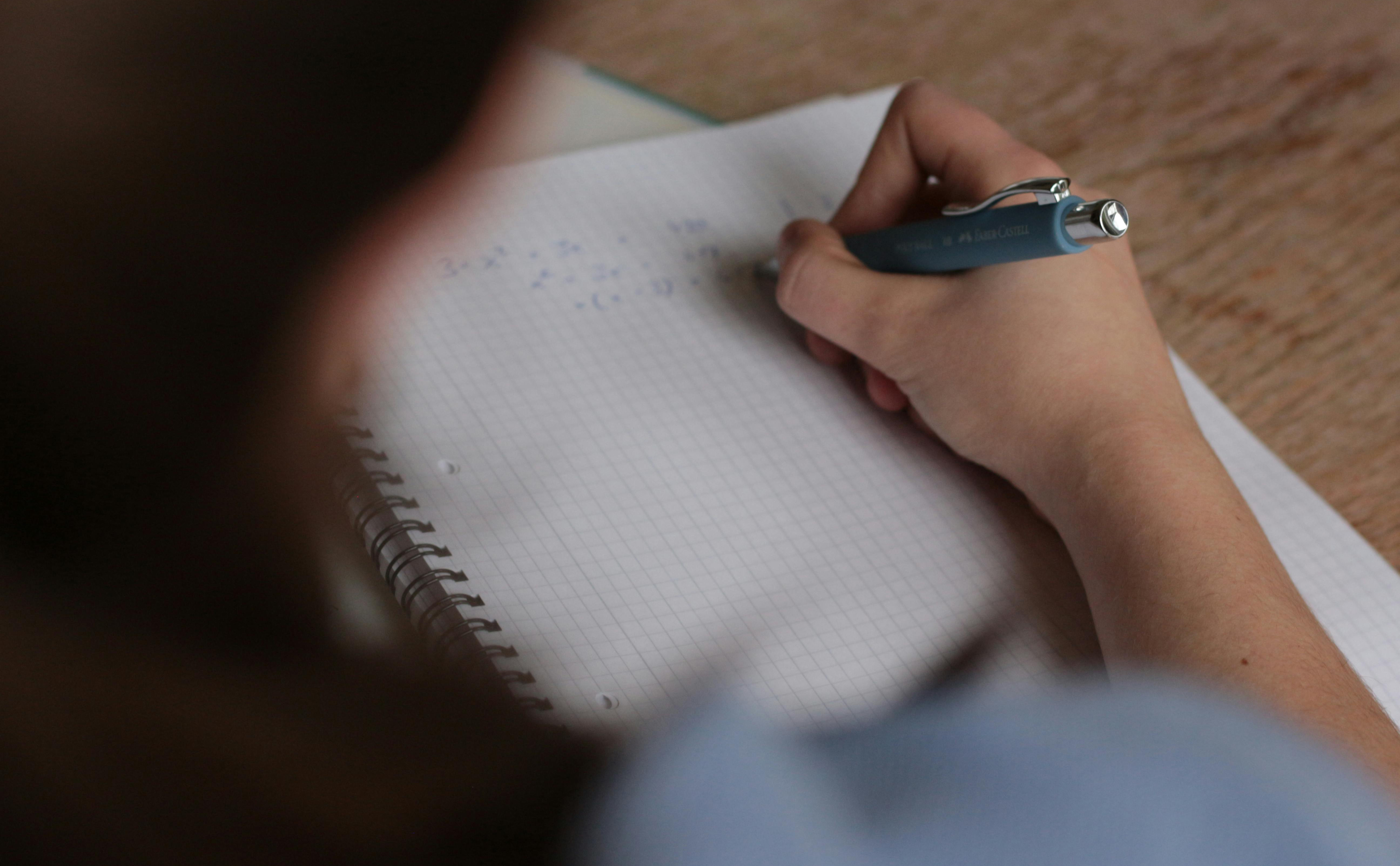 Person’s head, arm and hand, seen from behind, writing a maths equation on a pad of paper.