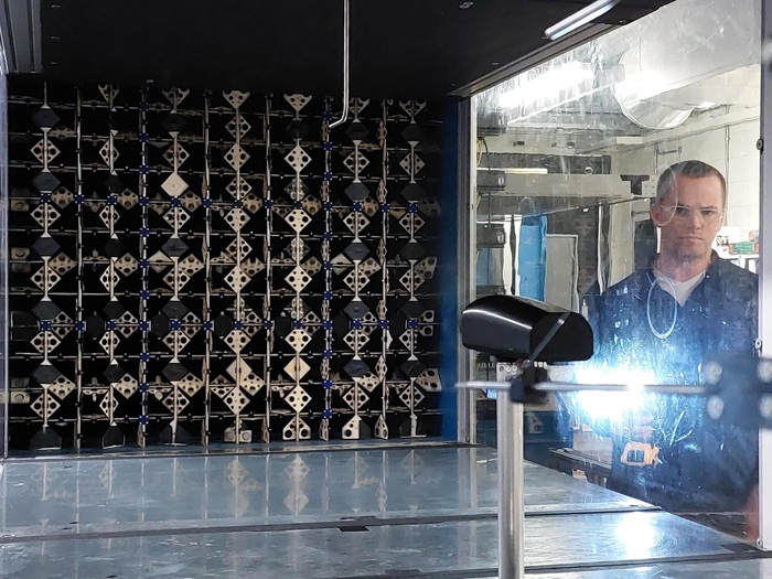 A man standing in front of active turbulence grid installed in a wind tunnel test section for controlled airflow experiments