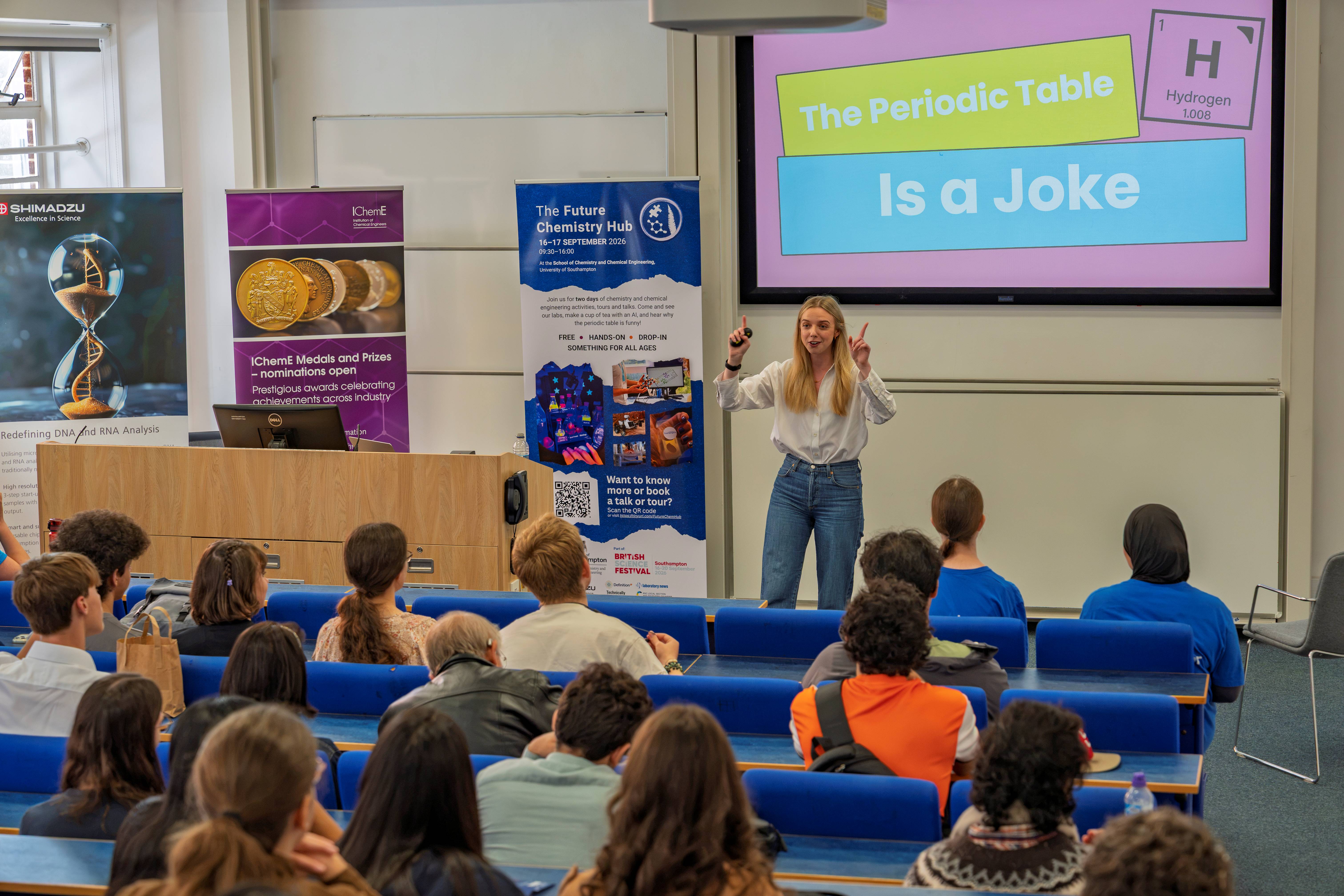 A presenter stands at the front of a lecture theatre speaking to an audience at the Future Chemistry Hub talks.