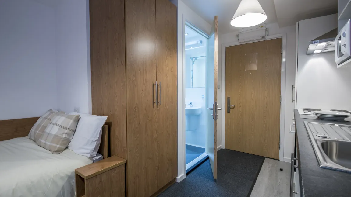 A modern studio flat showing bed, kitchenette and entrance to bathroom.