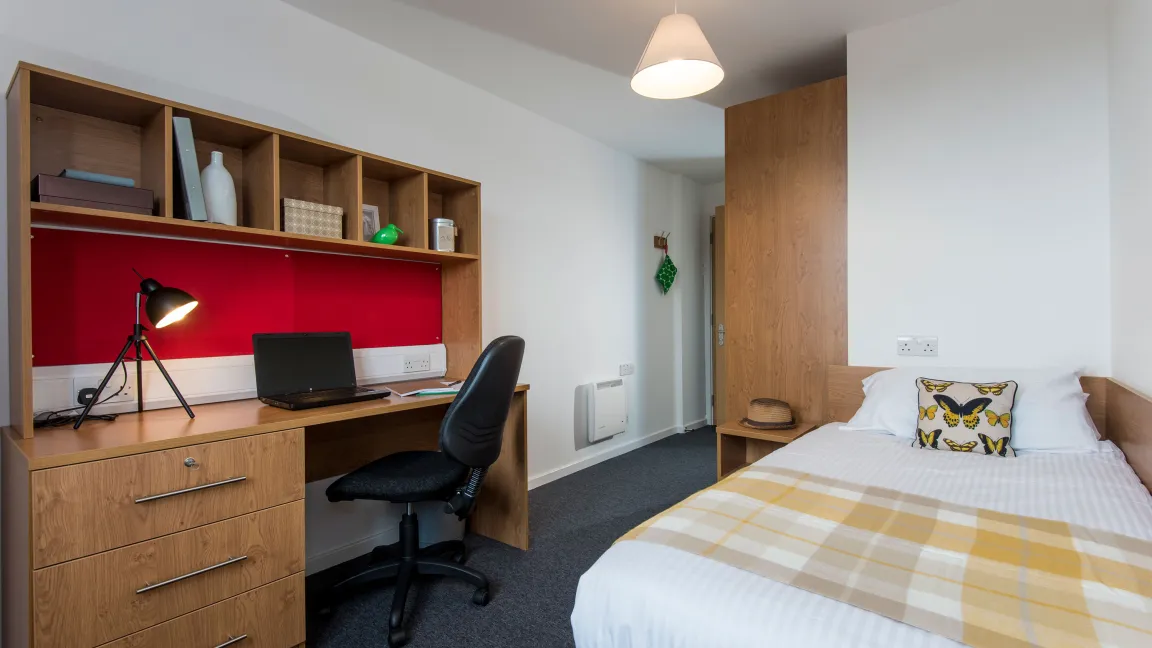 A modern student bedroom with white walls, wooden desk and neatly made double bed.