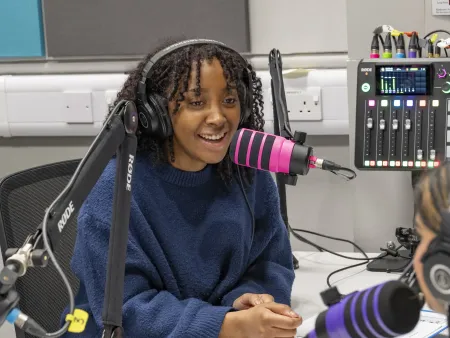 Olivia Coker, BA Film, TV and Digital Media student in a recording studio interviewing 2 other students. All 3 students have headphones on and a large microphone in front of them. 