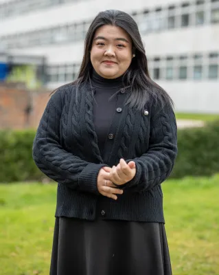 Xinyang Han is standing outside the University buildings, smiling at the camera.