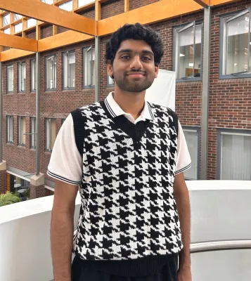 Elvin Jinu, Aeronautical and Astronautical Engineering student standing on the balcony of one of the Universities’ modern buildings with brick and wood features.