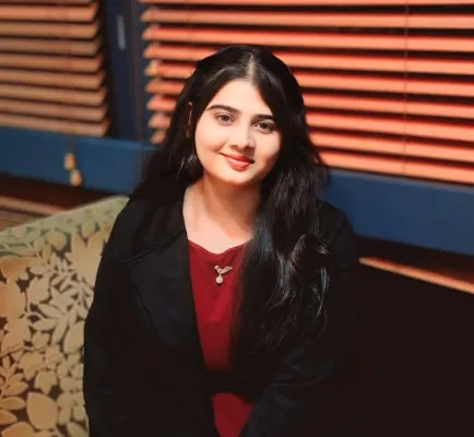 MSc Data and Decision Analytics student, Marwa Ashfaq is sitting down smiling at the camera. There is a closed window blind behind her.