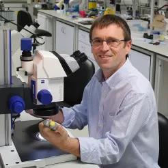 Professor Hywel Morgan sitting in front of a microscope in a lab.
