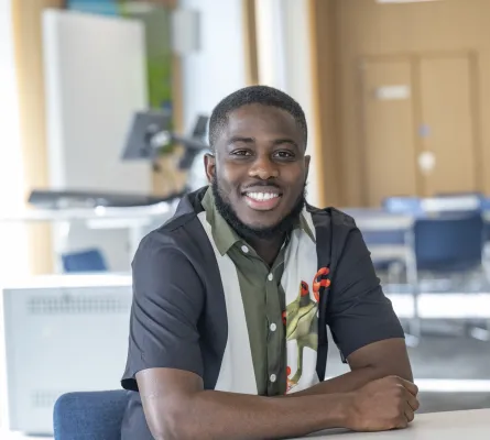 Applied GIS and Remote Sensing master’s student Bright, is sitting at a desk and smiling at the camera.