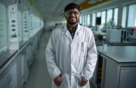 Advanced chemical engineering student Shantanu, wearing a white coat and safety glasses standing in a chemistry lab.