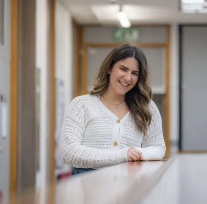 Psychology master’s student Zara is leaning on a table and smiling at the camera.