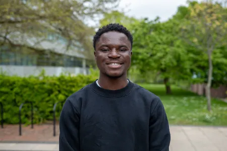 An image of David smiling for the camera. He's outside on the University of Southampton campus and there are green trees in the background.