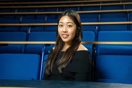 Student sitting in a lecture theatre, smiling at the camera.