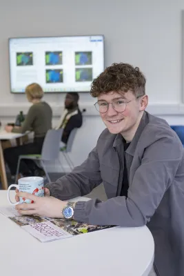 Samuel sat at a table in a communal area smiling for the photo.