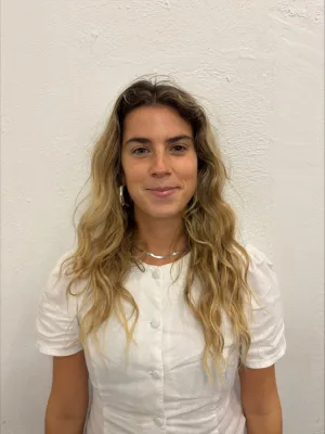 A headshot of a student with long blonde hair, wearing a silver necklace and a white top.