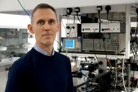 Dr Giorgio Adamo standing infront of electronic equipment in his lab.