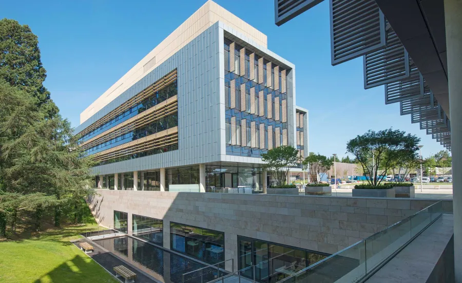 Exterior shot of modern building, surrounded by grass and trees, on a sunny day.