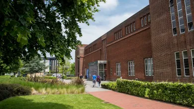 Exterior shot of academic building, trees and grass on a sunny day.