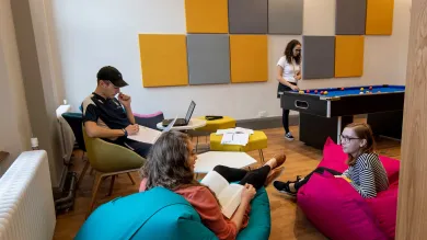Group of students in common room, sat talking and playing pool.