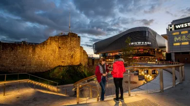 Two students stood on steps overlooking a paved plaza area with large buildings and shops.
