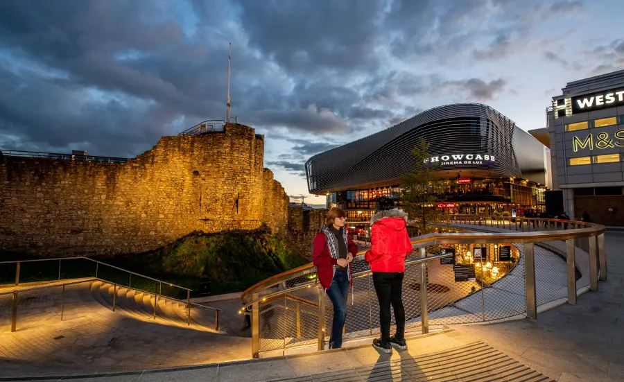 Two students stood on steps overlooking a paved plaza area with large buildings and shops.