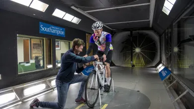 Man on bike in wind tunnel with man adjusting his wheel.