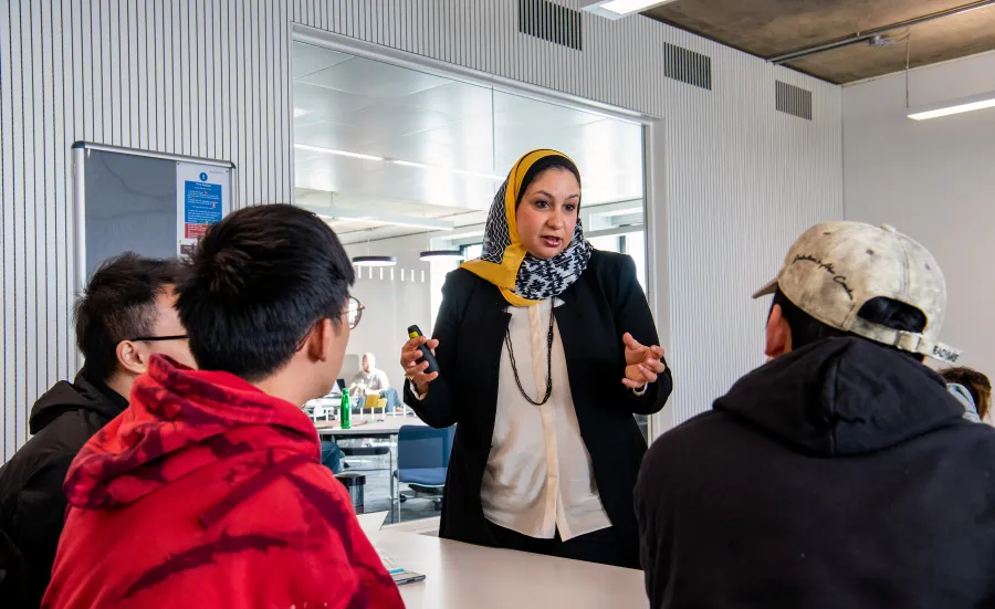 Lecturer talking to 3 students in a classroom. 