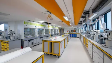 A large, modern, vibrant chemistry laboratory. The lab is empty, but a variety of glassware, fume cupboards and scientific equipment are visible.