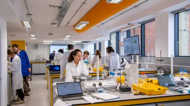 Group of students working in a bright, modern, vibrant chemistry laboratory. Students tend to a variety of equipment and glassware on the benches.