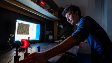 A student conducts an experiment in a dark laboratory, using a computer and some technical equipment on a large desk.