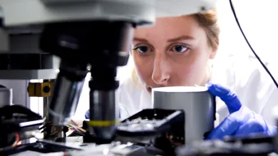 A female researcher peering intently at the contents of a slide in a high-powered microscope.