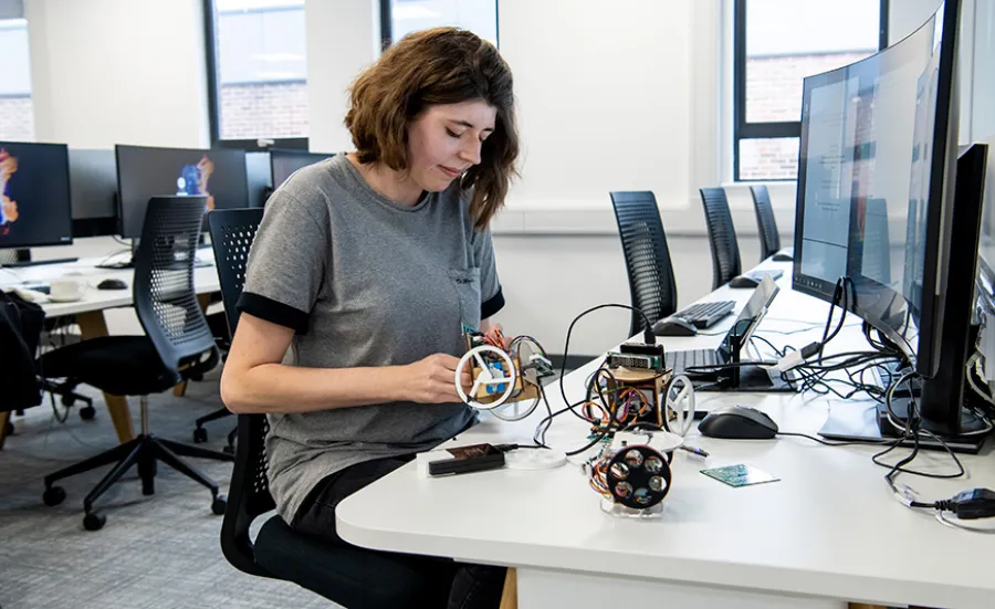 A student tinkers with the electronic components of a small robot while sat at a workstation in the lab.