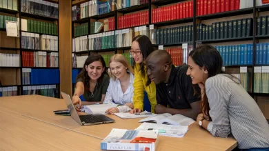 Students huddle around laptop in the library law collection