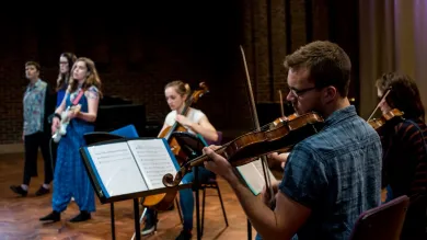 A violinist in foreground with musicians behind performing in Turner Sims