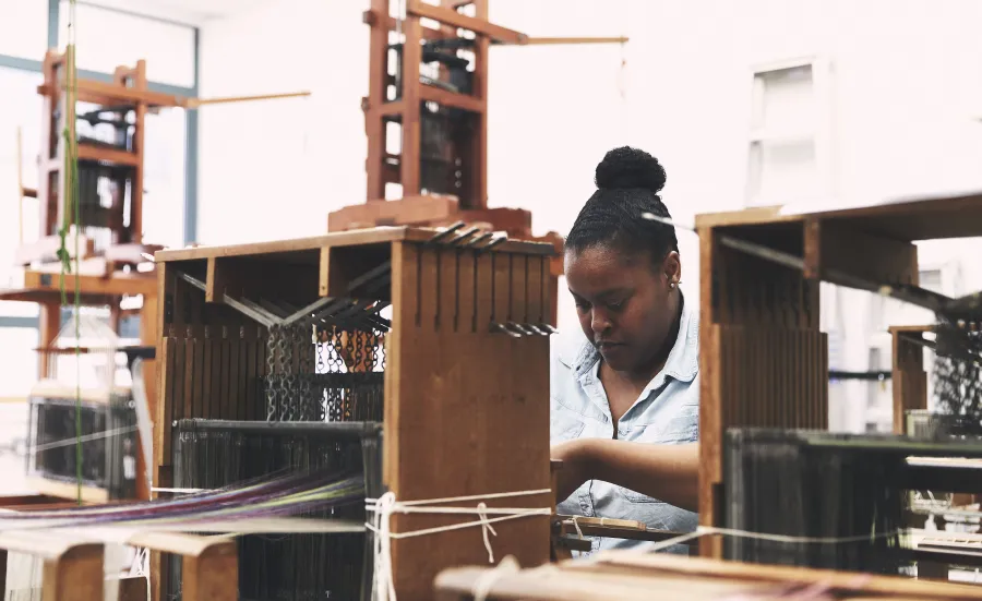 A student weaving at a wooden loom.