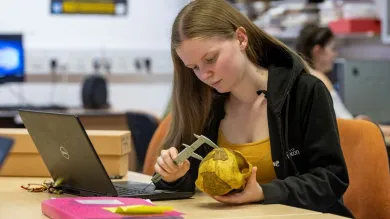 An archaeology student examines an object at a table, using a measuring device
