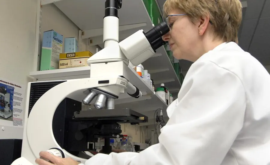 Person in lab coat using light microscope with digital camera attachment