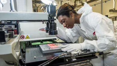 A student wearing protective clothing uses printed electronics and materials equipment