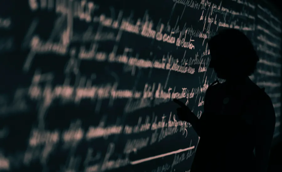 Stock image of a researcher's silhouette set against a wall projection of written language.