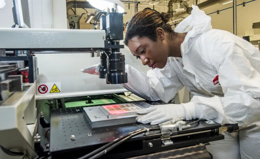 A PhD student leaning over to carefully observe a sample of printed electronics in the lab.