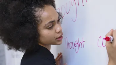 A student writes on a white board with a red marker in a lesson