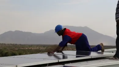 person wearing construction clothing fitting solar panels for renewable energy on roof in kenya