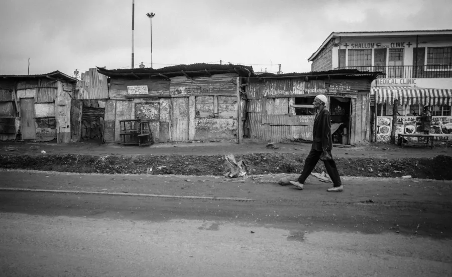 A black and white image of an elderly gentleman walking past a row of businesses in Nairobi, Kenya.