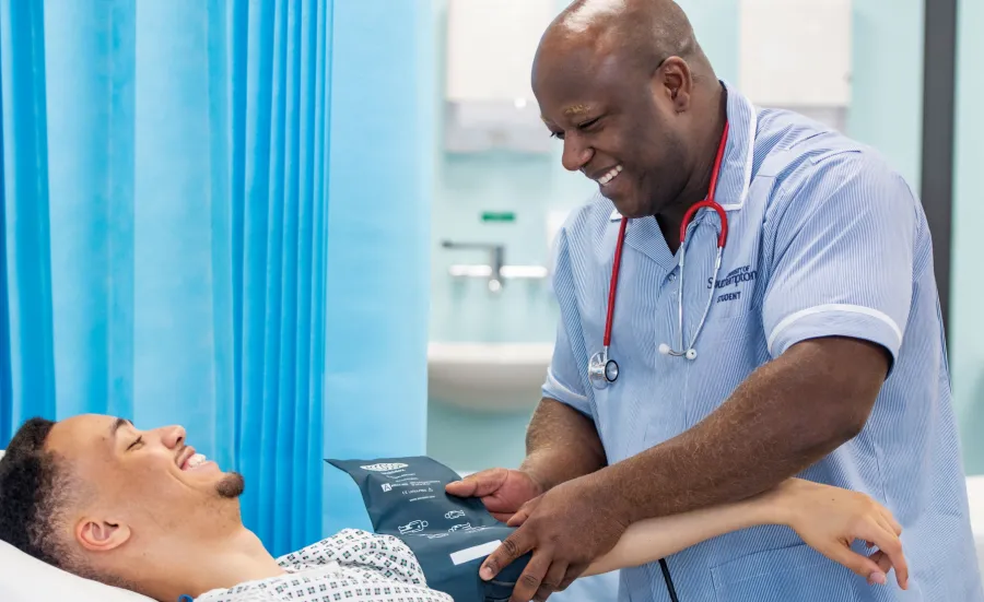 A patient and Southampton student nurse smiling at each other in a hospital room, as the nurse takes the patient's blood pressure.