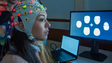 A study participant wears an EEG cap and is seated close to a screen displaying data.