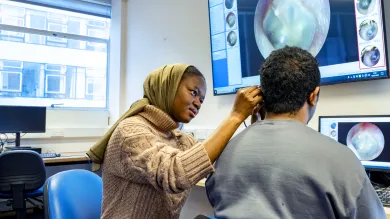 Audiology student looking into a persons ear and showing it on a big screen