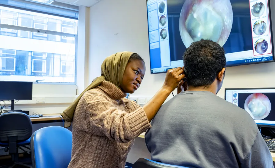 Audiology student looking into a persons ear and showing it on a big screen