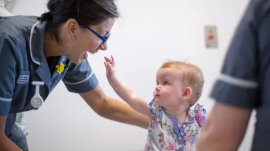 Baby reaches up towards smiling research nurse 