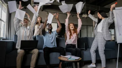 A diverse group of business people throw sheets of paper in the air