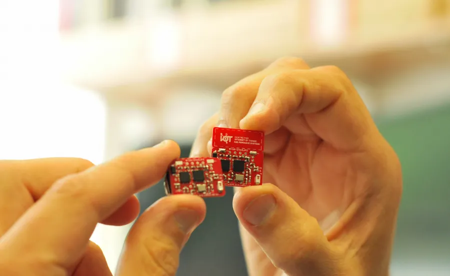 Hand holding a red internet of things circuit board created by the Centre for IoT and Pervasive Systems.