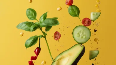 Half an avocado, halved cherry tomatoes, a red sliced chili pepper, basil leaves, cucumber slices and fine herbs fly into the air against a yellow background