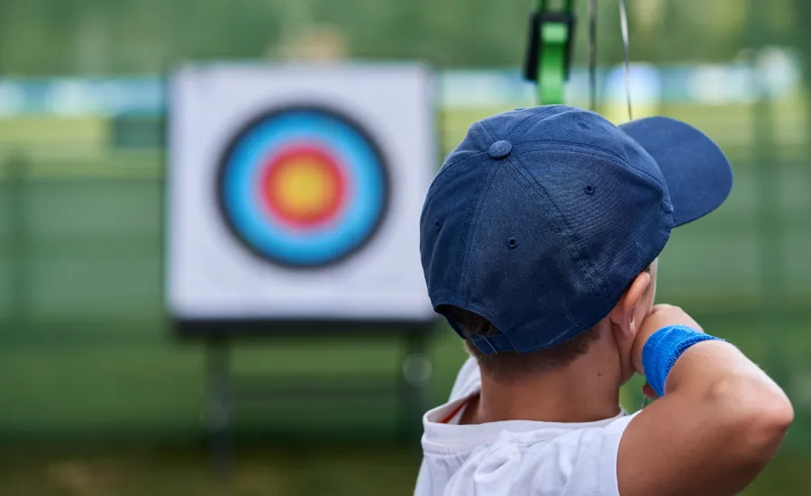 Close up of a child, seen from behind, about to shoot an arrow at an archery target.